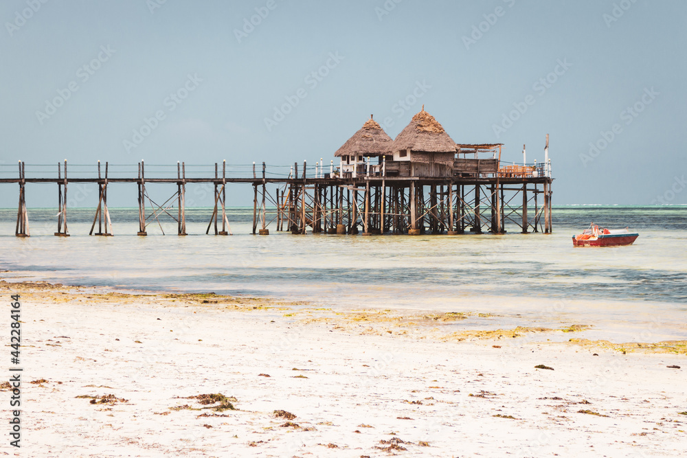 Wooden pier with boat and beach hut on sunny day. Low tide of Indian Ocean. Idyllic exotic resort. Pier in perspective with bungalows. Tropical paradise. Honeymoon in lagoon. Scenic tranquil seascape. Wooden pier with boat and beach hut on sunny day. Low tide of Indian Ocean. Idyllic exotic resort. Pier in perspective with bungalows. Tropical paradise. Honeymoon in lagoon. Scenic tranquil seascape.