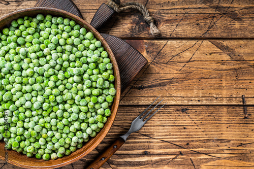 Cold Frozen green peas in a wooden plate. Wooden background. Top view. Copy space