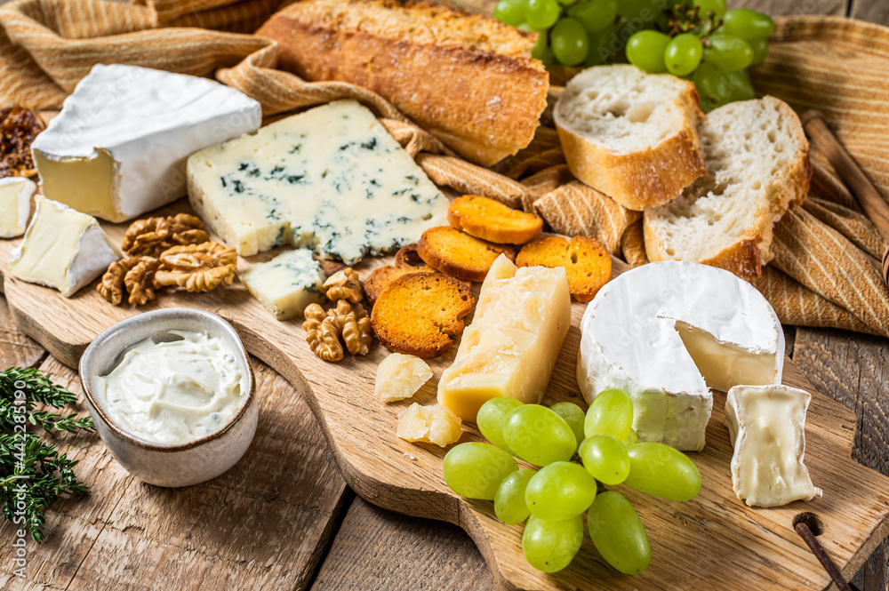 Cheese Board. Brie, Camembert, Roquefort, parmesan and blue cream cheese with grape, fig, bread and nuts on wooden board. wooden background. Top view