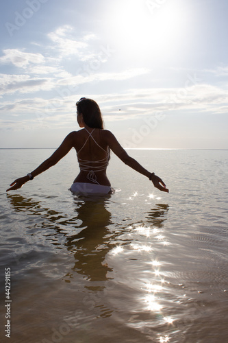 A girl from the back in a white swimsuit enters the sea sparkling from the sun