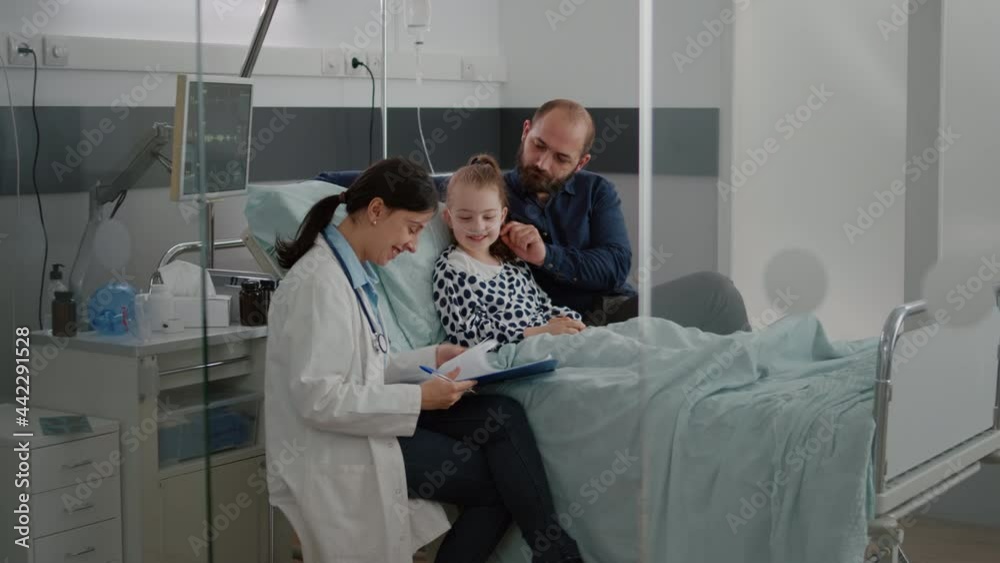Physician woman doctor monitoring disease symptoms writing antibiotics treatment during recovery consultation in hospital ward. Hospitalized child with nasal tube recovering after breathing surgery Physician woman doctor monitoring disease symptoms writing antibiotics treatment during recovery consultation in hospital ward. Hospitalized child with nasal tube recovering after breathing surgery