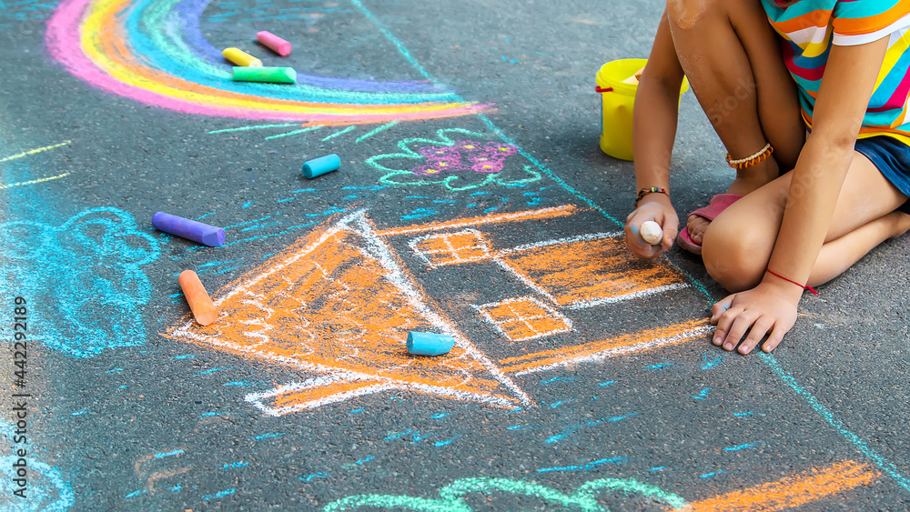Fototapeta premium The child draws a house and a rainbow on the asphalt with chalk. Selective focus.