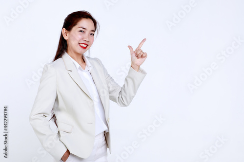 Confident young Asian businesswoman in stylish light suit smiling and pointing finger at blank space against white background.