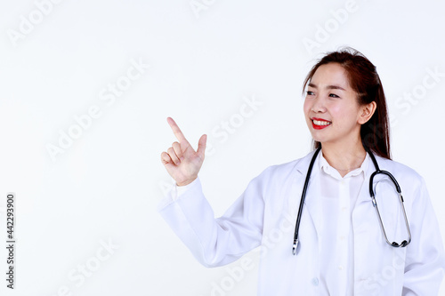 Happy young Asian female medic in uniform with stethoscope pointing aside at blank space on white background while advertising medical service
