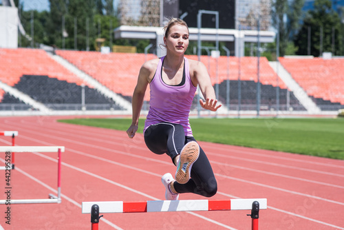 Woman athlete jumping over an obstacle. Running with hurdles. Active lifestyle