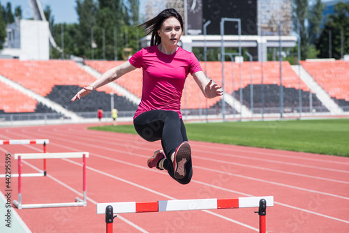 Woman athlete jumping over an obstacle. Running with hurdles. Active lifestyle