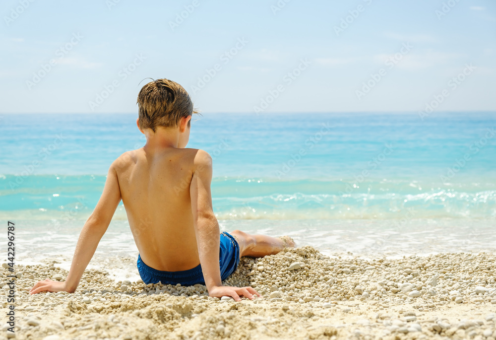 Young boy sitting on a beautiful beach during summer vacation in Greece