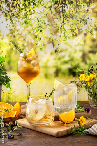 Three colorful summer cocktails on the table. Hard seltzer cocktails with various fruits: pear, orange and lemon. Summer party table outdoor in a house backyard with сold summer drinks.