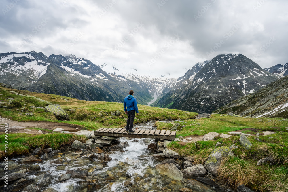 Man hiker resting on small bridge over mountaian river at Schlegeis Lake, Zillertal Alps, Austria