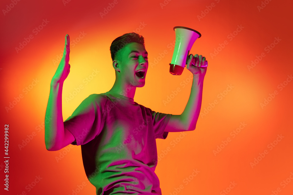 Portrait of Caucasian young man shouting with joy isolated on orange studio background in neon light. Concept of human emotions, facial expression. Portrait of Caucasian young man shouting with joy isolated on orange studio background in neon light. Concept of human emotions, facial expression.