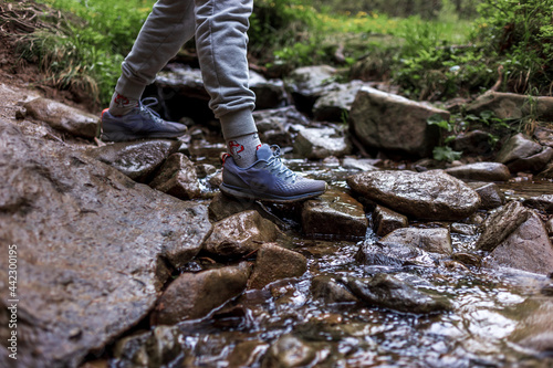 Close up of woman's shoes hiking in the mountains. Woman legs hiking at mountain wood. Outdoors crossing rock stones on river creek. Female travel on nature landscape.