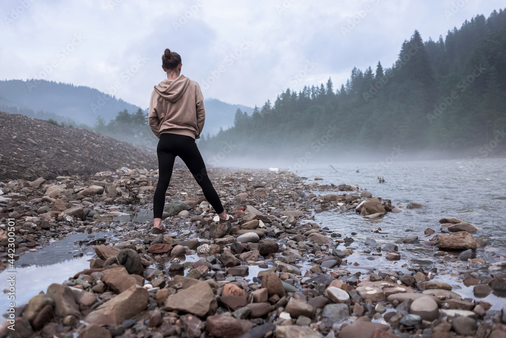 Woman in casual clothes walks on the rocks on the river in the mountains. Woman tourist walks on the fireplace on the forest river smoke on the water copy space Woman in casual clothes walks on the rocks on the river in the mountains. Woman tourist walks on the fireplace on the forest river smoke on the water copy space