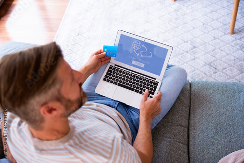 Man sitting on the couch at home and banking online on laptop. Rear view photo.