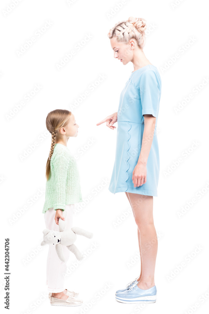 Vertical full length isolated side view shot of young adult woman scolding her daughter for being naughty, white background Vertical full length isolated side view shot of young adult woman scolding her daughter for being naughty, white background