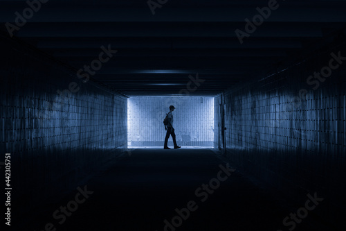 Dark underground passage with a silhouette of a man in profile in cold colors.