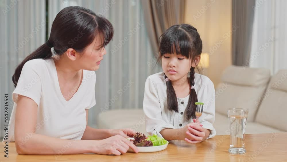 Asian Mother teach young girl child eat vegetable on table in house. Asian Mother teach young girl child eat vegetable on table in house.