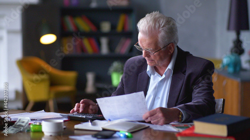 Senior man with papers or bills counting on calculator at home  photo