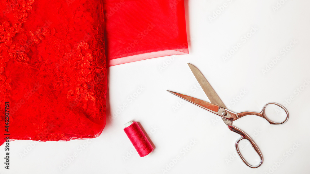 tailoring concept. elegant fabric white guipure on red satin with scissors and spool on white background tailoring concept. elegant fabric white guipure on red satin with scissors and spool on white background