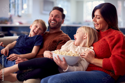 Family Sitting On Sofa With Popcorn Laughing Watching Comedy On TV Together