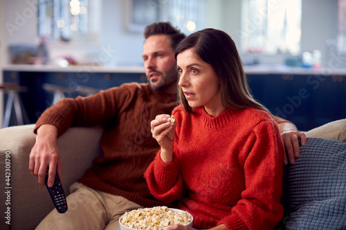 Couple Sitting On Sofa With Popcorn Watching Thriller On TV Together