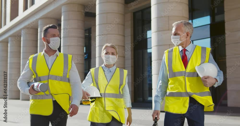 Team of engineers in protective mask walking outside office building Team of engineers in protective mask walking outside office building