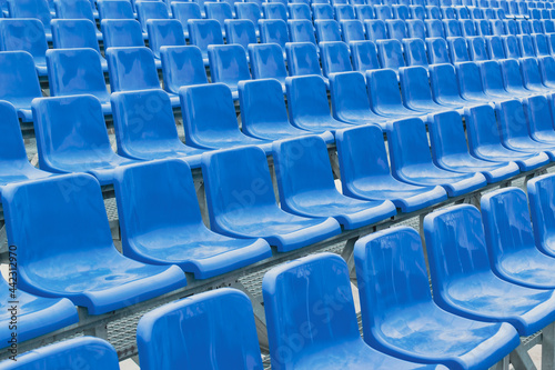 Empty tribune of a sports stadium. Blue plastic seats. Angle view. Light glare.