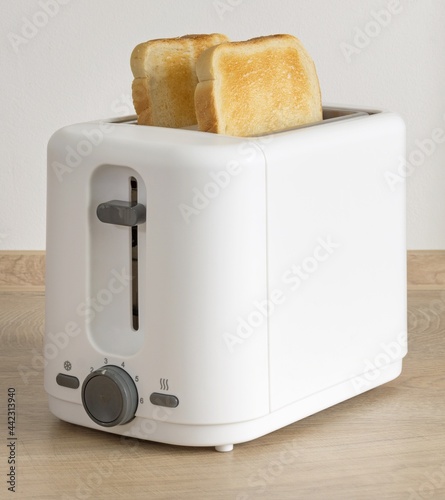 Two slices of golden brown toast in an electrical toaster on a wooden kitchen worktop table
