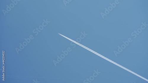 Passenger airplane at cruising altitude with contrail against blue sky photo