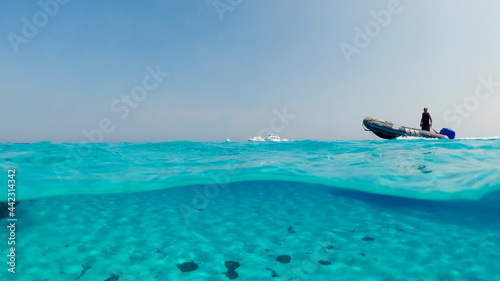 A motor boat in the ocean against the background of white yachts in the distance, you can see the bottom with white sand near the Underwater split reef