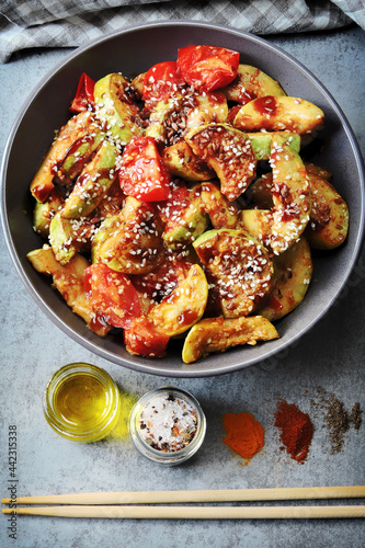 Fried zucchini slices in Asian style in a bowl with sesame seeds and vegetables.