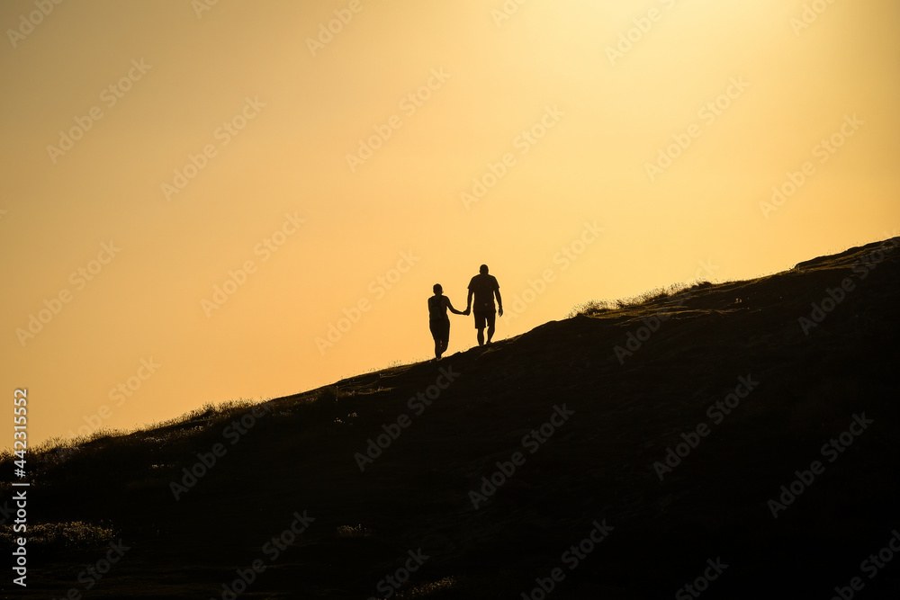 A couple holding hands walking towards a hill top to watch the sunset
