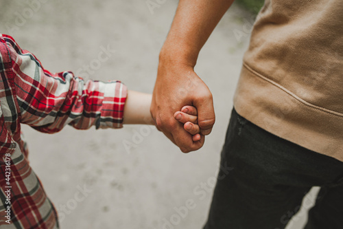 hands of father and child. father holds tightly small hand of cute unrecognizable child in checkered red shirt. taking care of children. strong family relationships. selective focus