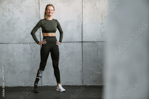 Young sportswoman with prosthesis smiling while working out indoors
