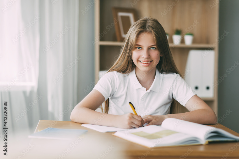 A smiling girl does her homework, writes a synopsis, and prepares for lectures. The concept of training and education A smiling girl does her homework, writes a synopsis, and prepares for lectures. The concept of training and education