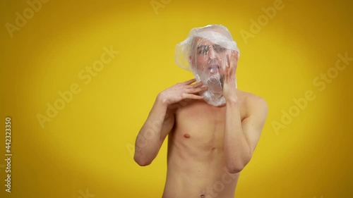 Portrait of young Caucasian man with plastic on head posing at yellow background. Male Caucasian queer person suffocating of social intolerance concept photo