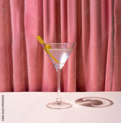 A glass of cocktail, martini in front of reach pink renaissance velvet curtain. Retro style theatre vibe.