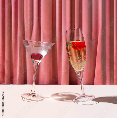 A glass of cocktail and a glass of champagne in front of reach pink renaissance velvet curtain. Dancing  glasses retro concept.