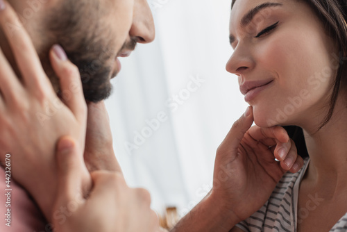 close up view of smiling young woman with closed eyes touching face of boyfriend with hands in kitchen