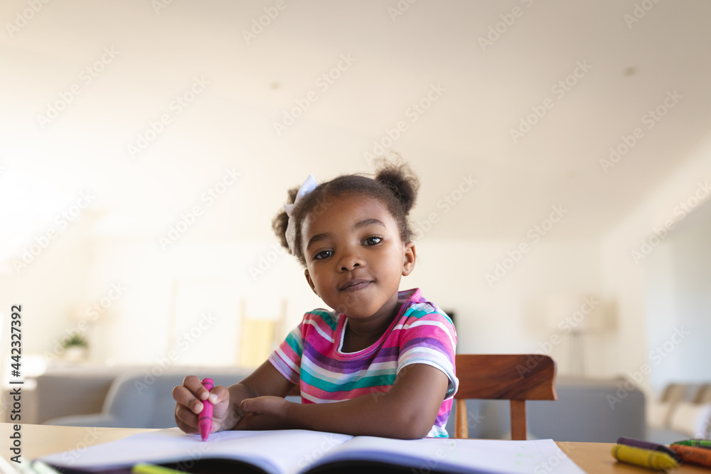 Portrait of happy african american girl sitting at dining table drawing in book, smiling to camera Portrait of happy african american girl sitting at dining table drawing in book, smiling to camera