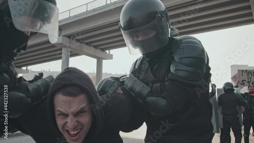 Slowmo tracking shot of riot police officers in full gear arresting screaming male protester