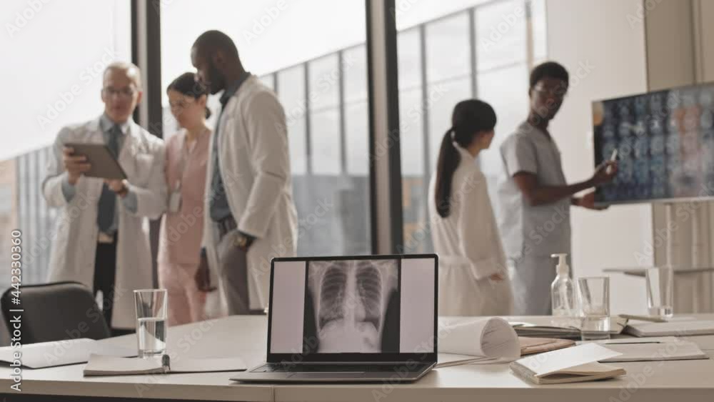 Medium slowmo of multiethnic group of radiologists consulting each other in modern clinic with chest x-ray on laptop screen in selective focus Medium slowmo of multiethnic group of radiologists consulting each other in modern clinic with chest x-ray on laptop screen in selective focus