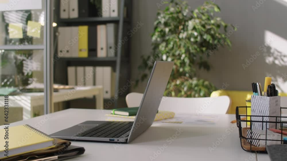 Arc shot of laptop and copybooks on desk in modern office with no people