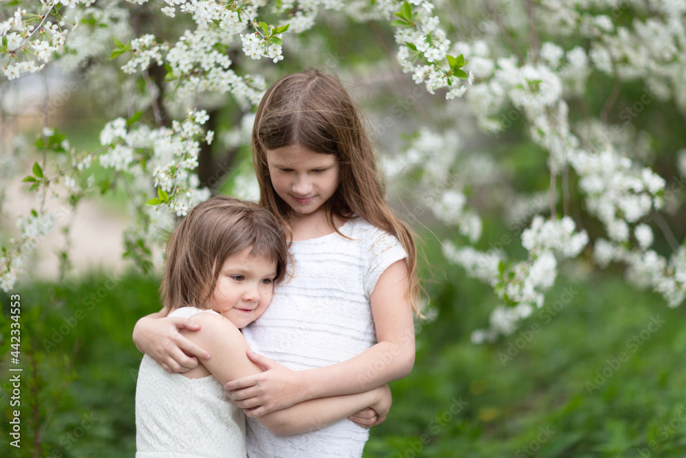 Cute little girls kids girlfriends hugging among the foliage and flowers, the concept of girlish friendship and secrets, childhood in summer Cute little girls kids girlfriends hugging among the foliage and flowers, the concept of girlish friendship and secrets, childhood in summer