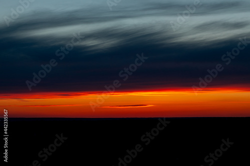 Dawn sunrise sunset is located in a stripe in a field on the horizon, the natural background of a beautiful bright colorful dramatic sky with clouds in red-yellow orange tones