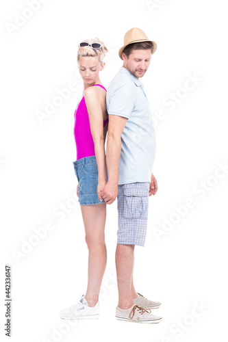 Vertical full length studio portrait of romantic young man and woman wearing summer outfits standing back to back holding hands, white background