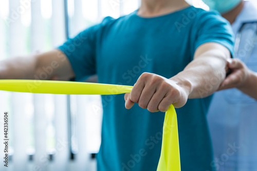 Physical therapist gives resistance band exercises. About the arms and shoulders of male office workers, office syndrome, male patient. Physiotherapy concept. © crizzystudio