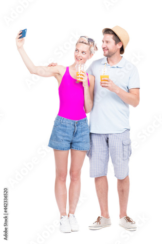 Vertical full length studio portrait of romantic young man and woman wearing summer outfits standing close to each other drinking fresh fruit juice