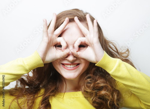 Cheerful curly woman looks through zero or ok gesture, holds rounded fingers near eye