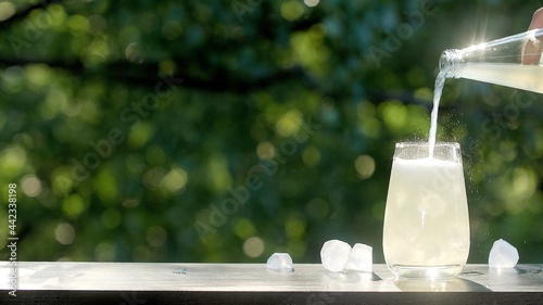 Making drinks outdoors. Hand pours a carbonated drink into a transparent glass with ice. Little splashes fly to the sides from a highly carbonated drink. Many ice cubes in a glass and around photo