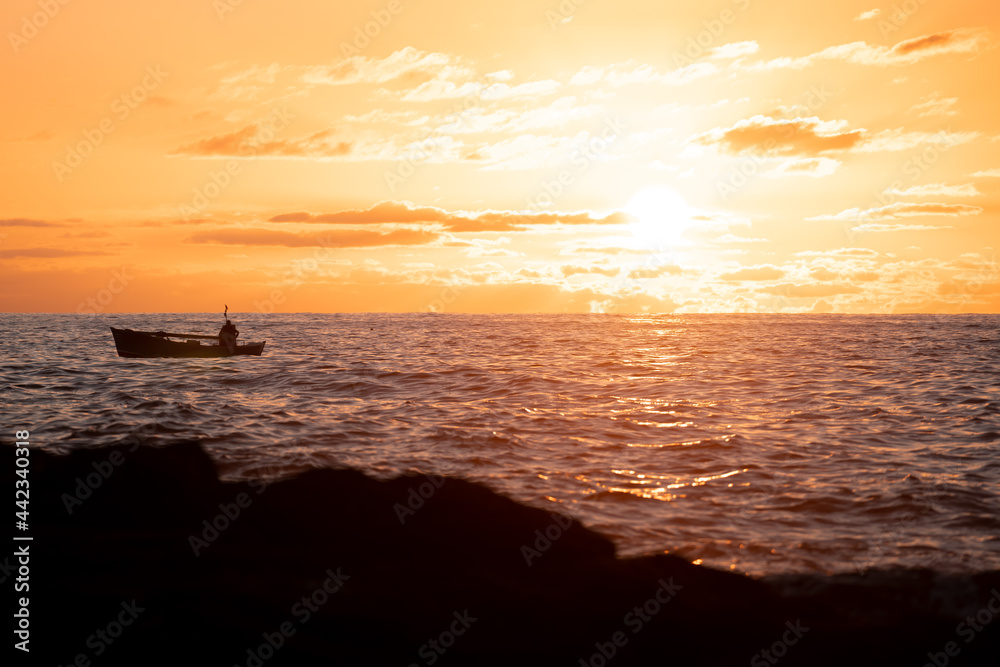A fisherman in his boat sails the sea at sunset time with a golden sky and clouds. Concept of peace, tranquility